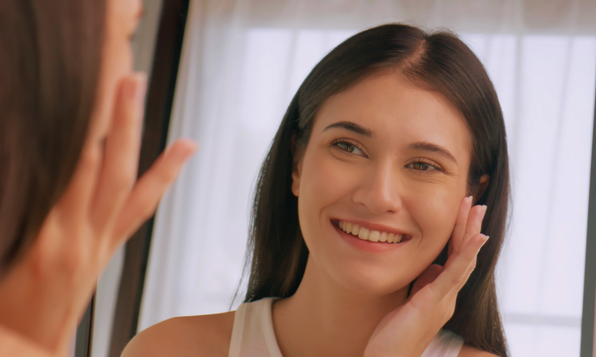 Smiling woman touching her cheek as she looks at herself in a mirror