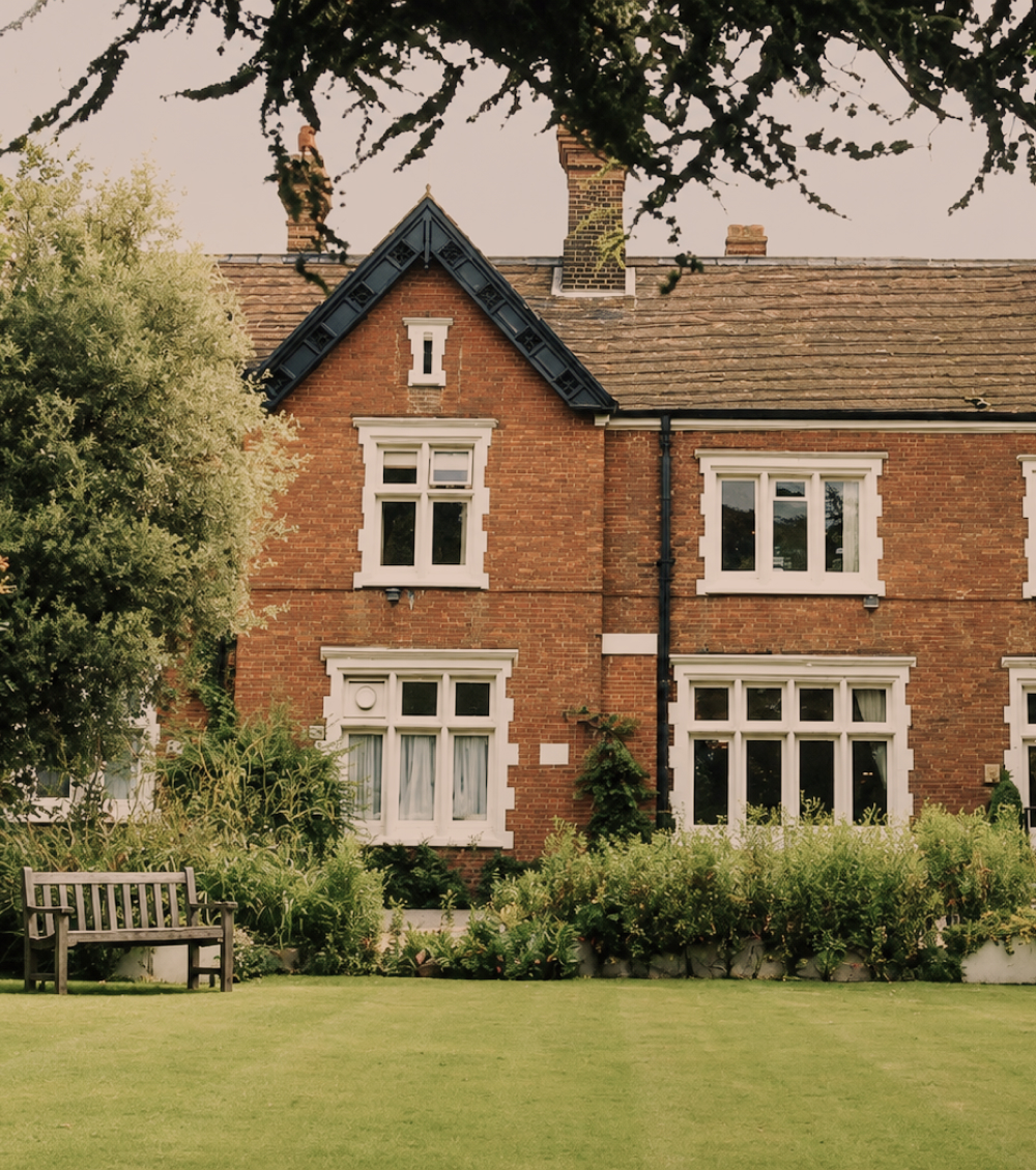 The exterior of The Holly Private Hospital, a low brick building set behind mature trees and a landscaped forecourt