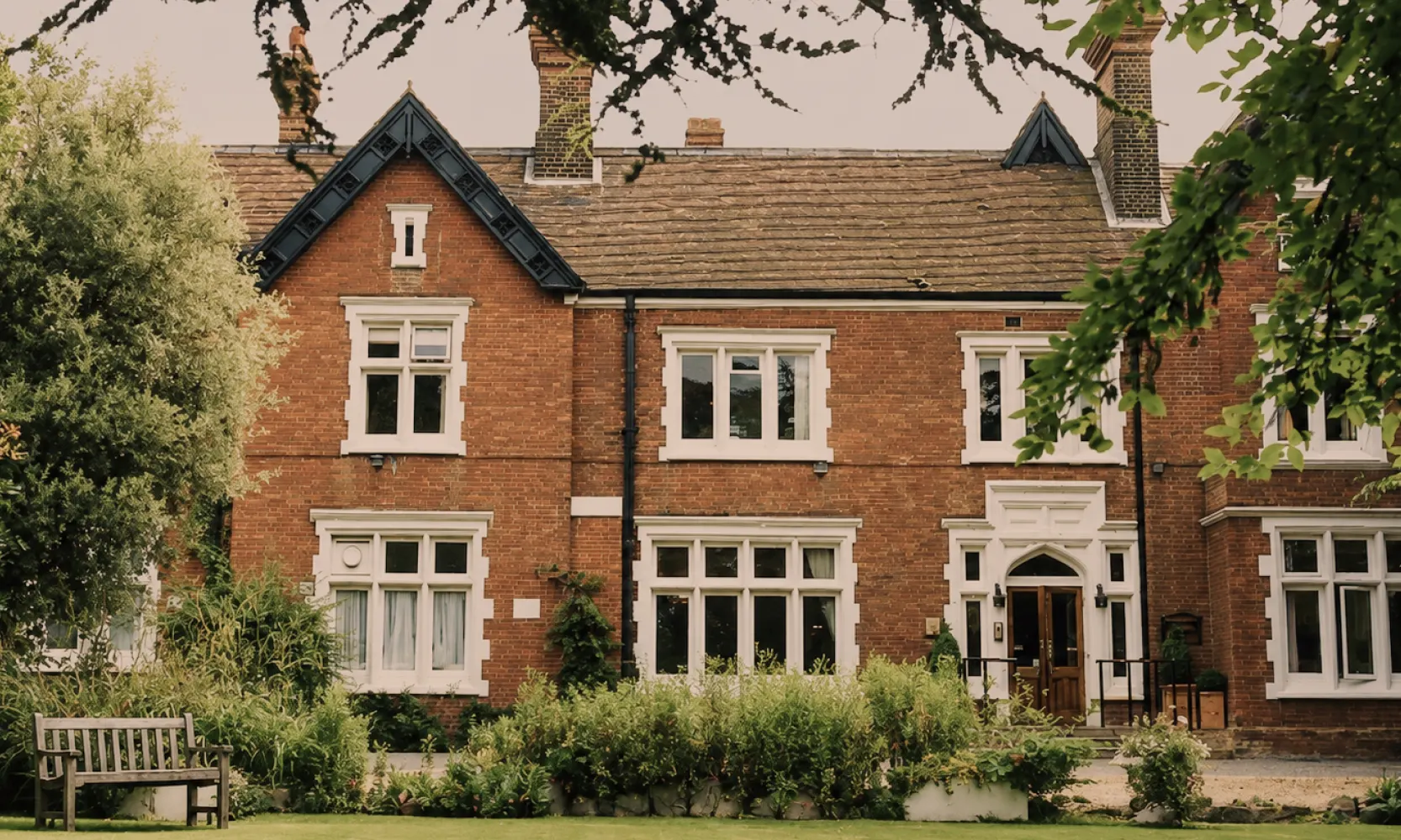 The exterior of The Holly Private Hospital, a low brick building set behind mature trees and a landscaped forecourt